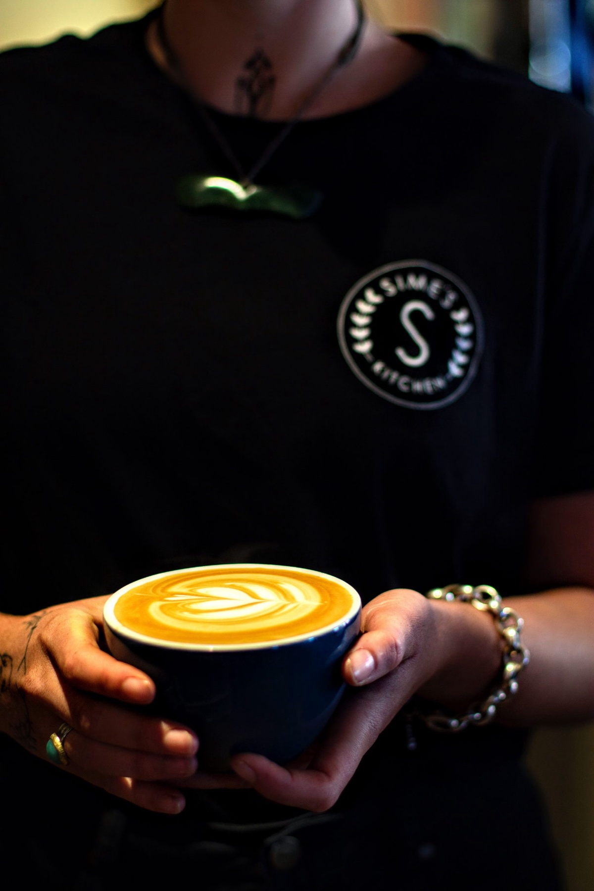 Sime's Kitchen barista Victoria presenting a blue cup of freshly poured flat white
