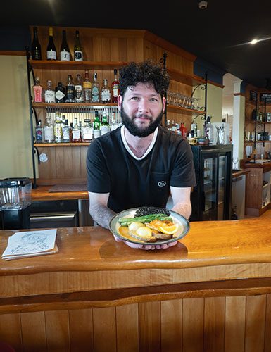 Owner Sam McConnochie holding a breakfast plate behind the bar